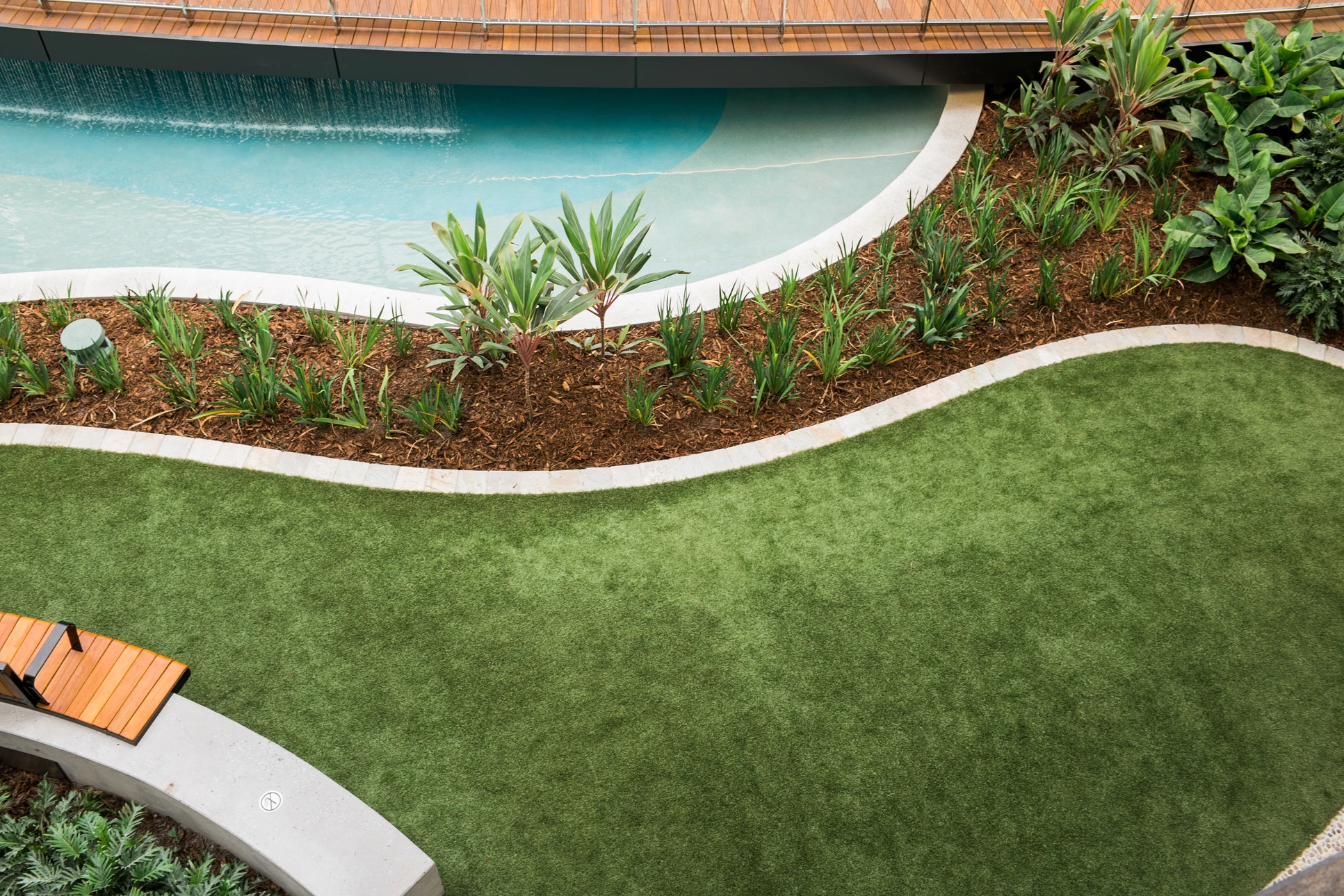 Aménagement paysager extérieur avec piscine turquoise, gazon synthétique impeccable et massifs végétalisés